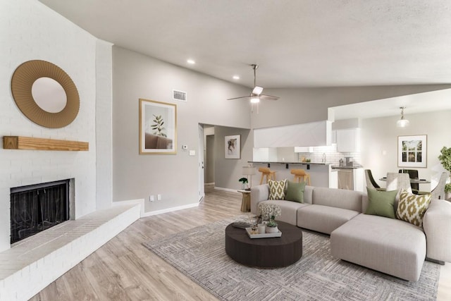 living area with lofted ceiling, a fireplace, visible vents, baseboards, and light wood-style floors