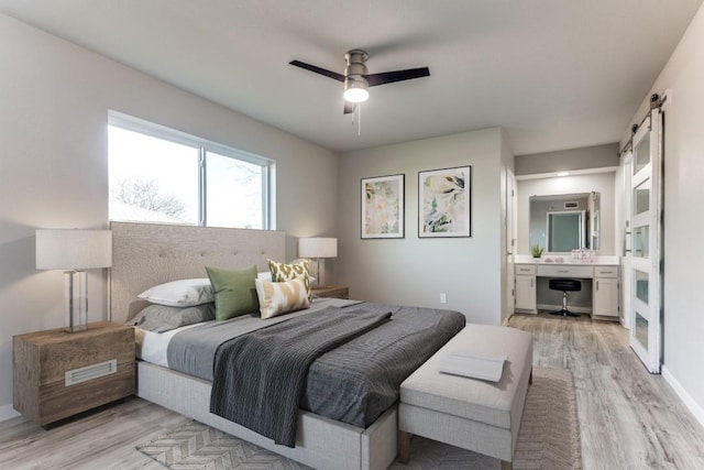 bedroom featuring ceiling fan, a barn door, ensuite bath, and light wood-style floors