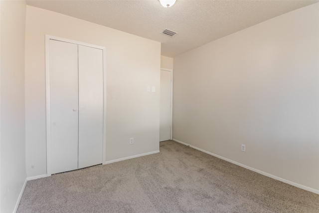 unfurnished bedroom with a closet, light carpet, and a textured ceiling