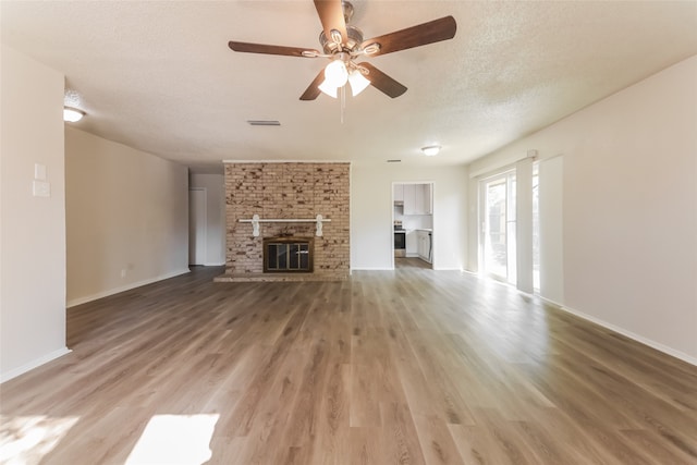 unfurnished living room featuring a textured ceiling, ceiling fan, wood-type flooring, and a brick fireplace