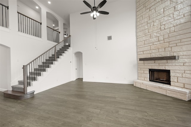 unfurnished living room featuring a stone fireplace, ceiling fan, a towering ceiling, and dark wood-type flooring