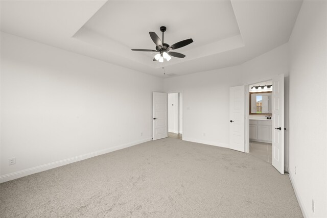 unfurnished bedroom with a raised ceiling, ensuite bath, ceiling fan, and light carpet