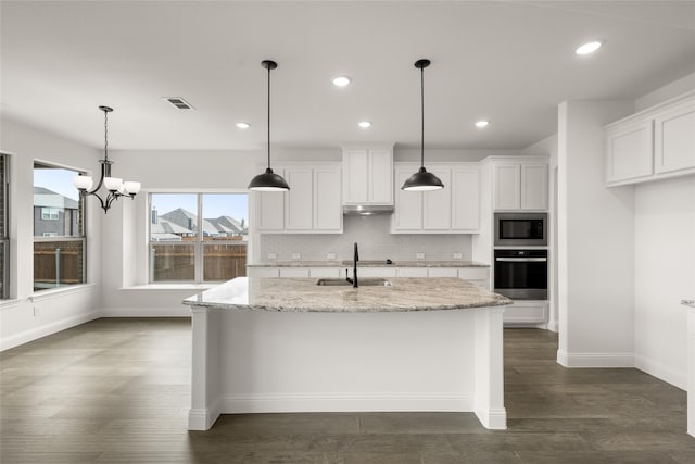 kitchen featuring light stone countertops, white cabinetry, stainless steel appliances, and a kitchen island with sink