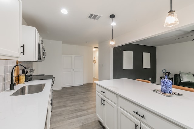 kitchen with light hardwood / wood-style floors, white cabinetry, tasteful backsplash, and hanging light fixtures