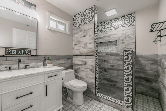 bathroom featuring a tile shower, toilet, tile walls, vanity, and tile patterned flooring