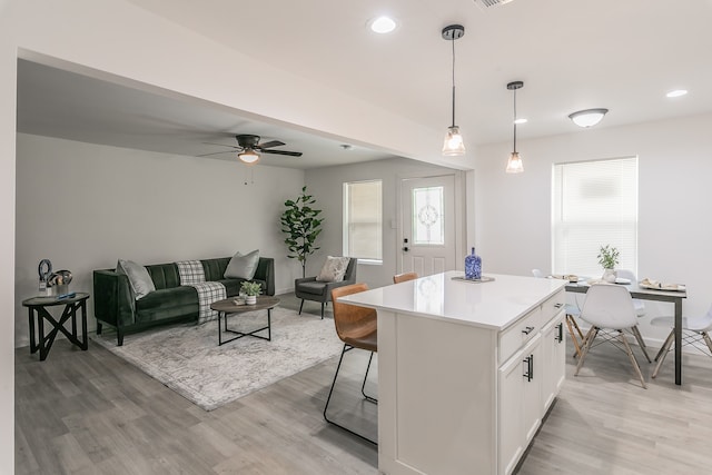 kitchen featuring a breakfast bar area, light hardwood / wood-style flooring, hanging light fixtures, a center island, and white cabinetry