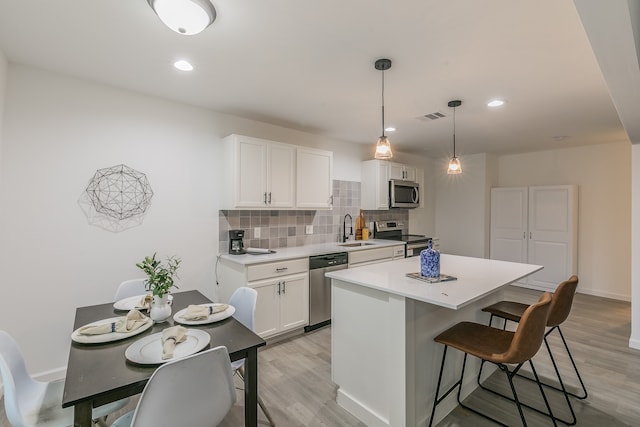 kitchen with white cabinetry, stainless steel appliances, light wood-type flooring, and decorative light fixtures