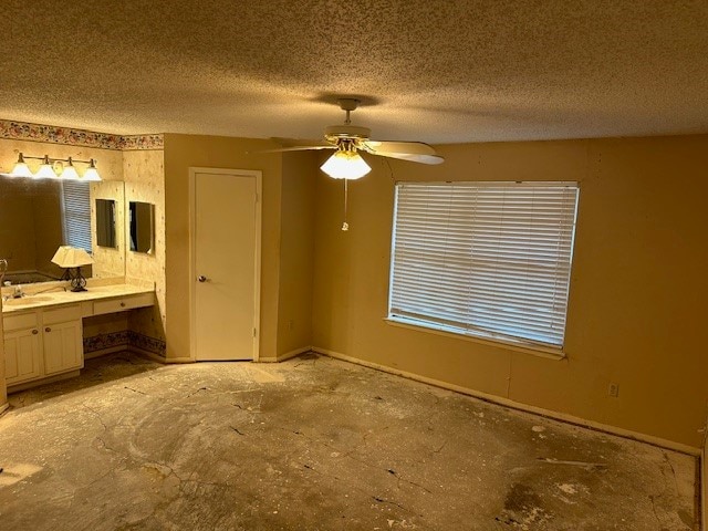 unfurnished bedroom with built in desk, ceiling fan, a textured ceiling, and ensuite bath