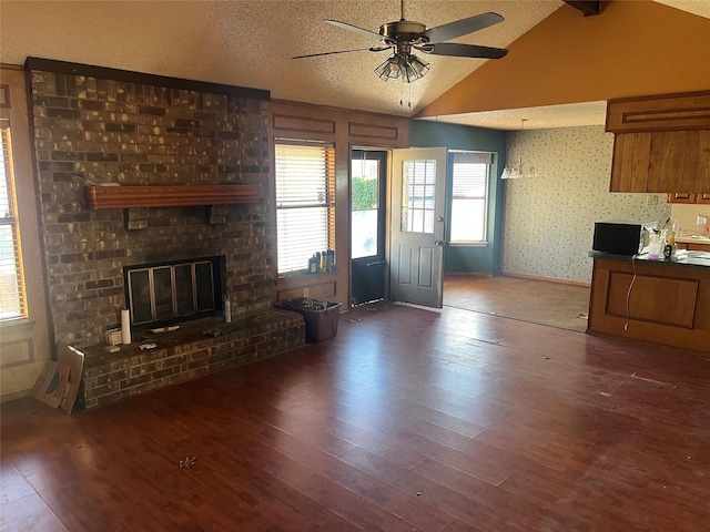 unfurnished living room with dark wood-type flooring, a textured ceiling, a fireplace, ceiling fan, and vaulted ceiling with beams