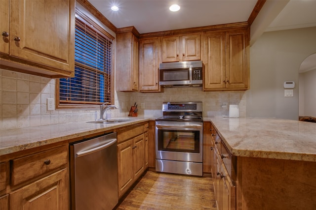 kitchen featuring decorative backsplash, light stone counters, sink, light hardwood / wood-style floors, and stainless steel appliances