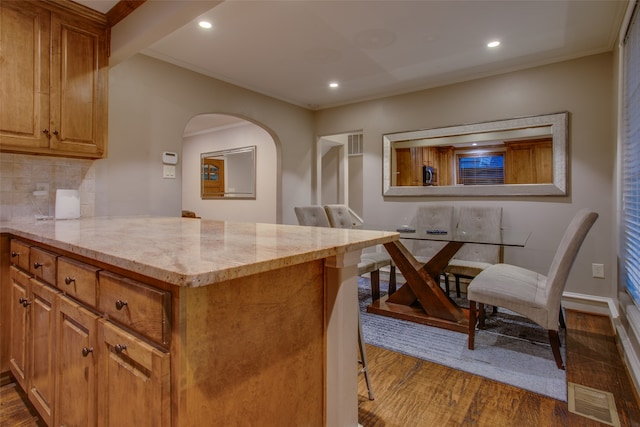 kitchen with light stone countertops, kitchen peninsula, wood-type flooring, and tasteful backsplash