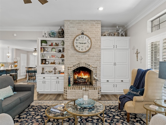 living room with light hardwood / wood-style floors, crown molding, a brick fireplace, and ceiling fan