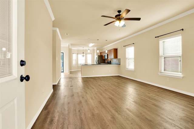 unfurnished living room with ornamental molding, ceiling fan with notable chandelier, a healthy amount of sunlight, and dark hardwood / wood-style flooring