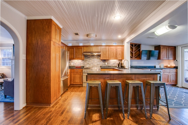 kitchen with hardwood / wood-style flooring, a breakfast bar area, backsplash, ornamental molding, and appliances with stainless steel finishes