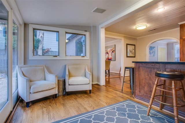 sitting room with light hardwood / wood-style flooring, ornamental molding, indoor bar, and vaulted ceiling