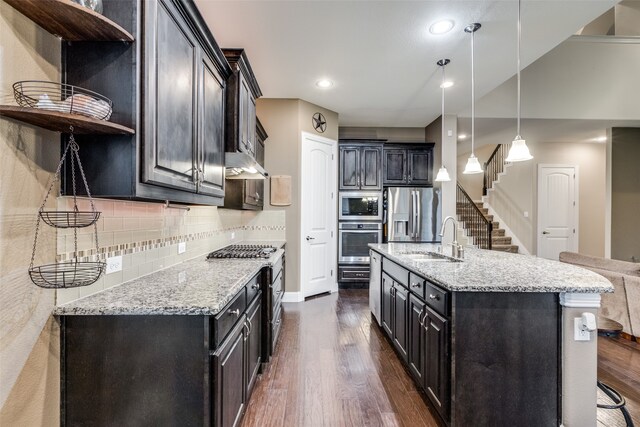 kitchen with light stone countertops, open shelves, a sink, stainless steel appliances, and dark wood-type flooring