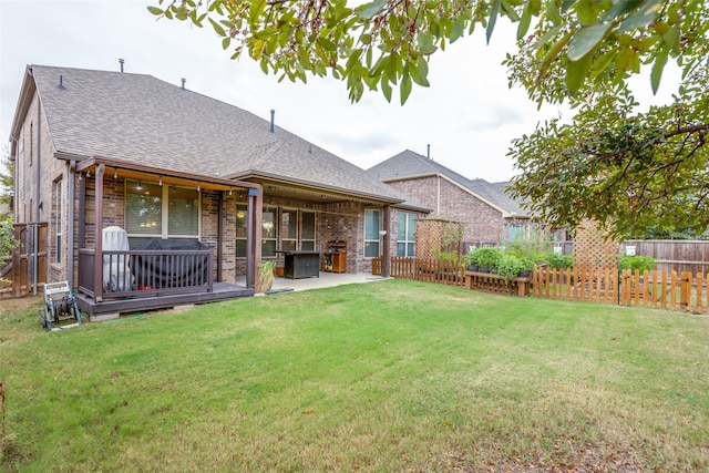 rear view of property featuring brick siding, a shingled roof, fence, a lawn, and a patio