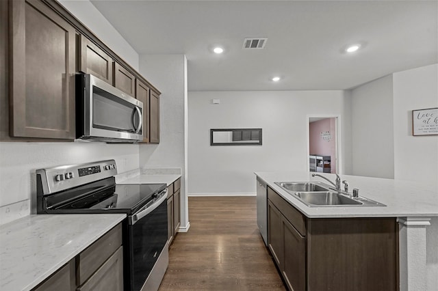 kitchen featuring dark wood-type flooring, stainless steel appliances, dark brown cabinets, a center island with sink, and sink