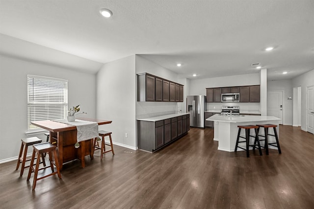 kitchen with dark brown cabinets, a center island with sink, a breakfast bar, dark hardwood / wood-style floors, and stainless steel appliances