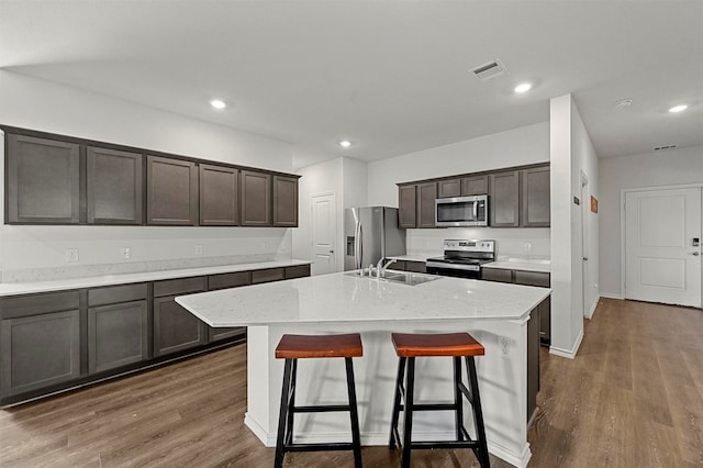 kitchen featuring appliances with stainless steel finishes, dark brown cabinets, an island with sink, and dark hardwood / wood-style flooring