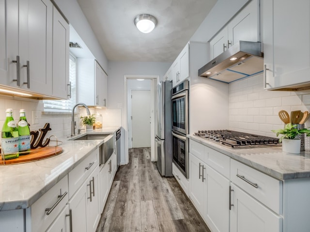 kitchen with light stone countertops, appliances with stainless steel finishes, sink, white cabinets, and light hardwood / wood-style flooring