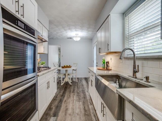 kitchen featuring dark hardwood / wood-style floors, stainless steel appliances, backsplash, white cabinetry, and light stone counters