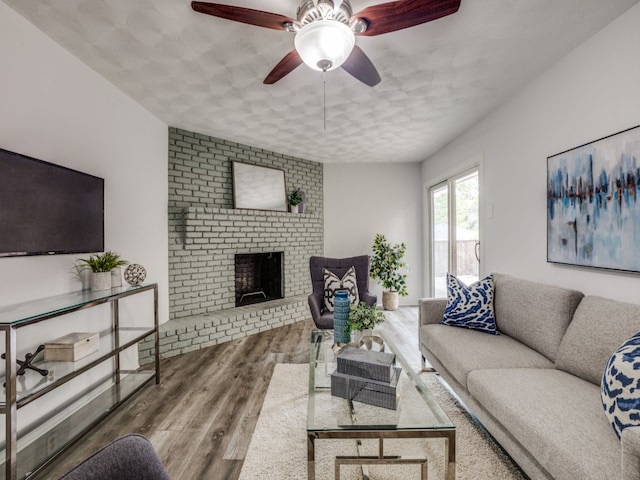 living room with ceiling fan, wood-type flooring, a textured ceiling, and a brick fireplace