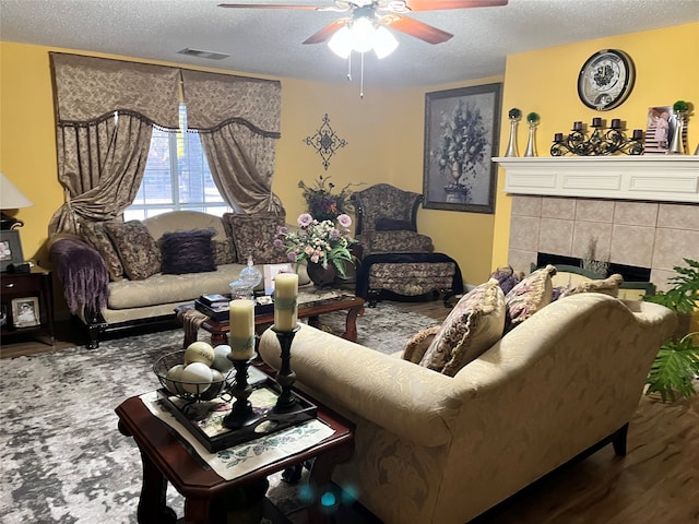 living room with ceiling fan, a textured ceiling, wood-type flooring, and a tile fireplace