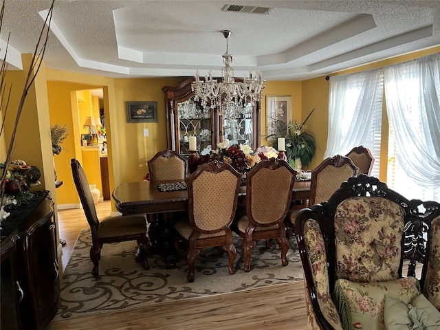 dining room featuring a notable chandelier, a textured ceiling, light wood-type flooring, and a raised ceiling