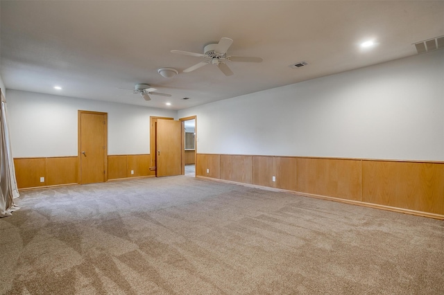 empty room featuring light carpet, ceiling fan, and wood walls