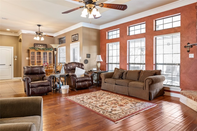 living room featuring ceiling fan, crown molding, hardwood / wood-style flooring, and a stone fireplace