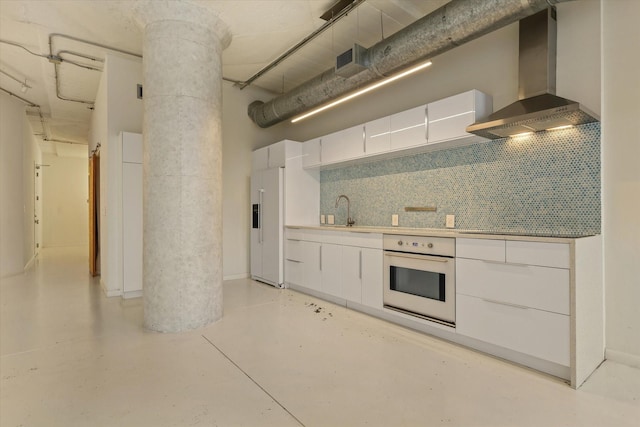 kitchen featuring white oven, paneled fridge, wall chimney range hood, and white cabinets