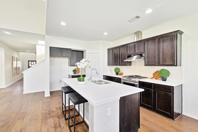 kitchen featuring sink, an island with sink, dark brown cabinets, stainless steel range with gas cooktop, and light hardwood / wood-style flooring