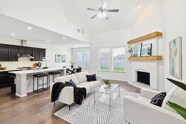 living room with ceiling fan, high vaulted ceiling, dark wood-type flooring, and a brick fireplace