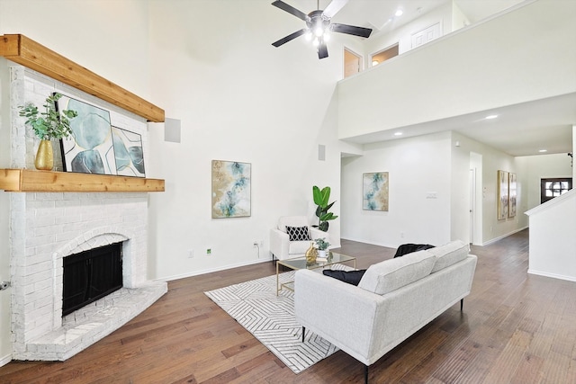 living room featuring dark wood-type flooring, ceiling fan, a towering ceiling, and a brick fireplace