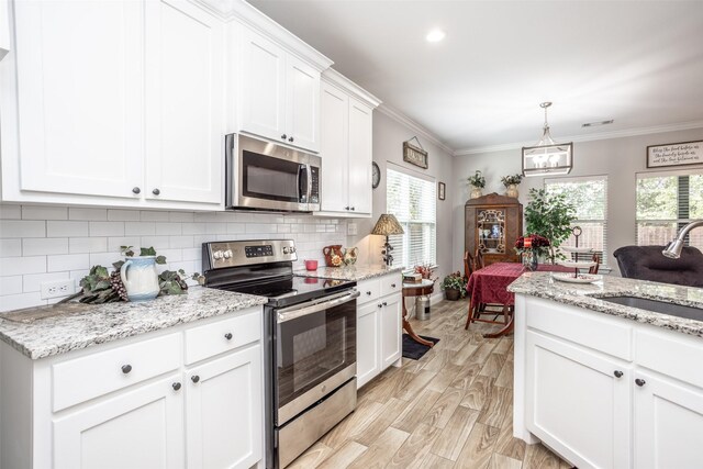 kitchen with kitchen peninsula, white cabinets, sink, crown molding, and stainless steel appliances