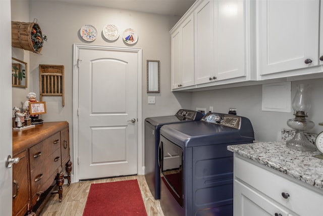 clothes washing area featuring separate washer and dryer, light wood-type flooring, and cabinets