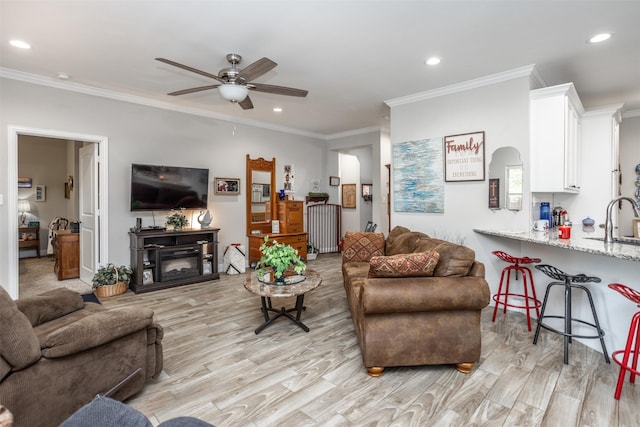 living room with crown molding, sink, ceiling fan, and light wood-type flooring