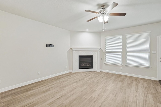 unfurnished living room with ceiling fan, a fireplace, and light wood-type flooring