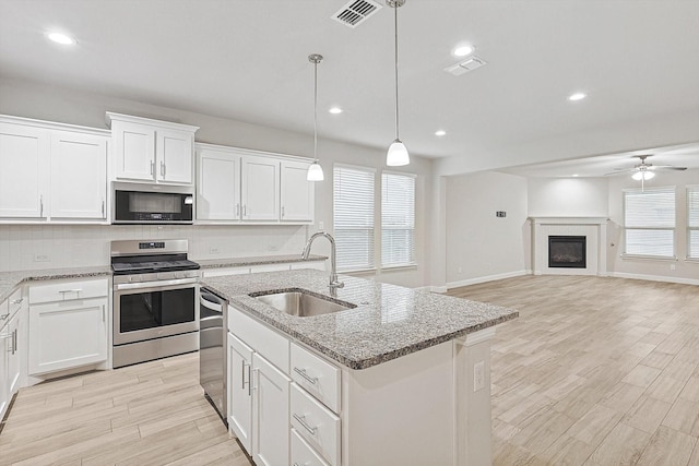 kitchen featuring sink, an island with sink, decorative light fixtures, white cabinets, and appliances with stainless steel finishes