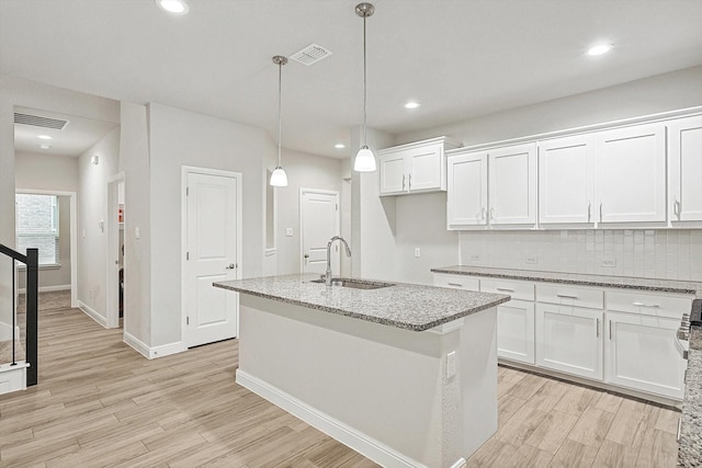 kitchen featuring white cabinets, a center island with sink, and sink