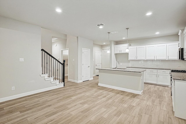 kitchen with dark stone counters, a center island with sink, white cabinets, hanging light fixtures, and tasteful backsplash