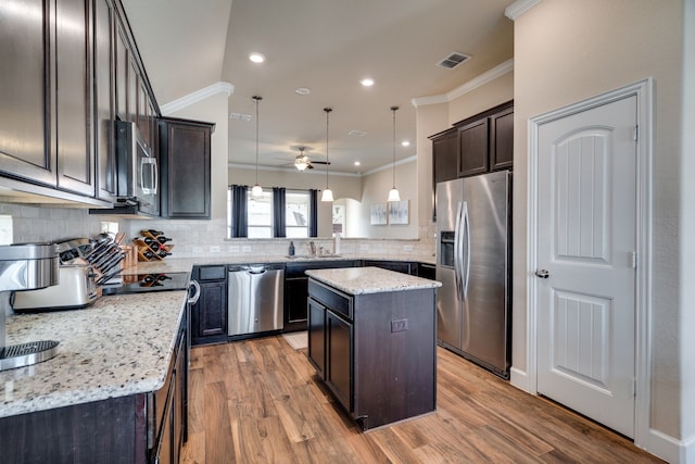 kitchen with pendant lighting, ceiling fan, light stone countertops, a kitchen island, and stainless steel appliances