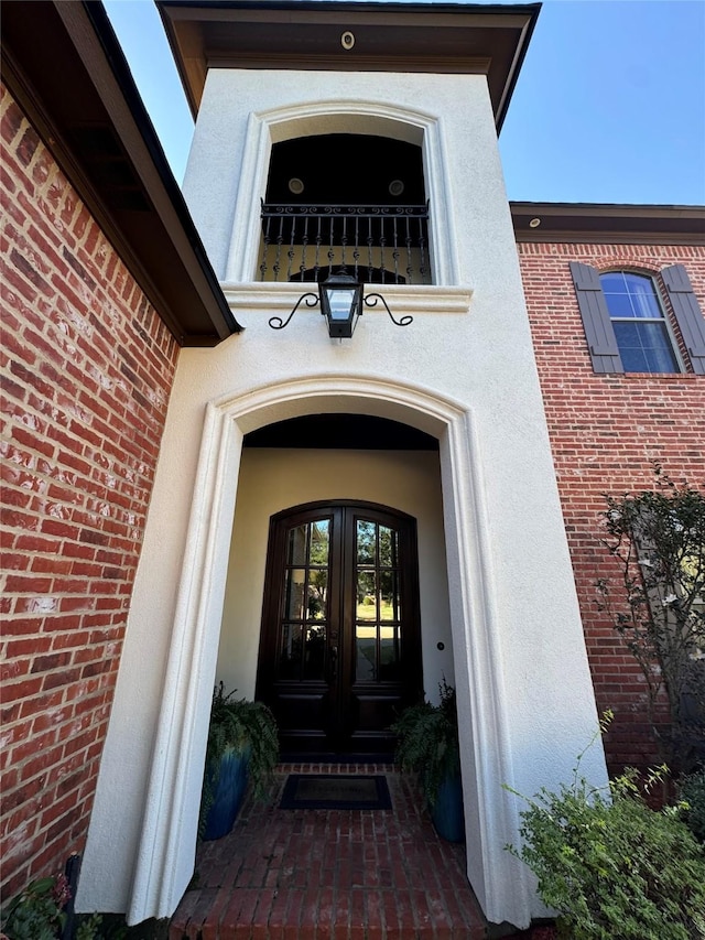 view of exterior entry with french doors, brick siding, and stucco siding