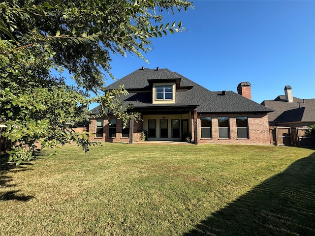 back of house with brick siding, roof with shingles, fence, and a yard