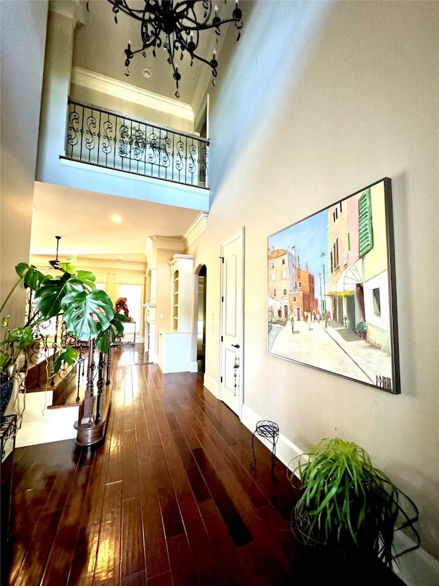 corridor with baseboards, arched walkways, a towering ceiling, wood finished floors, and crown molding