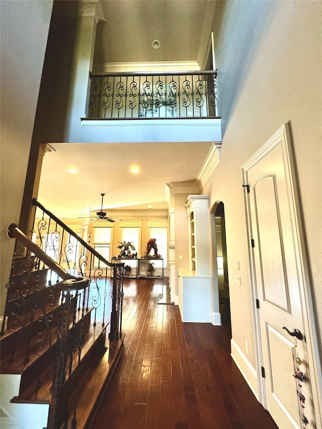 hall featuring baseboards, arched walkways, hardwood / wood-style flooring, a high ceiling, and crown molding