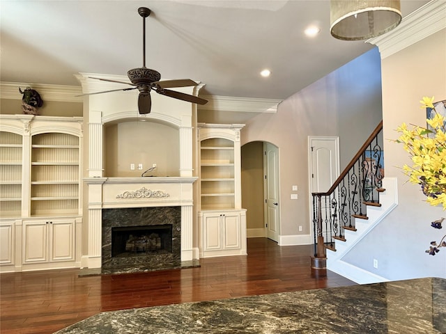 unfurnished living room featuring baseboards, hardwood / wood-style flooring, ceiling fan, a premium fireplace, and crown molding