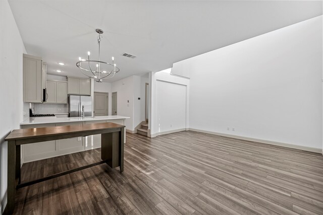 kitchen featuring backsplash, wood-type flooring, stainless steel refrigerator, gray cabinets, and decorative light fixtures