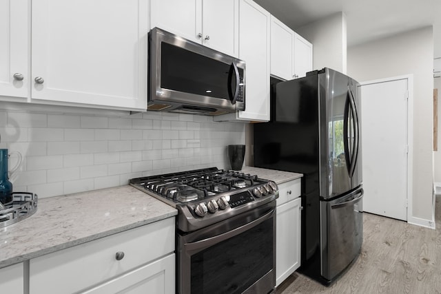 kitchen featuring decorative backsplash, appliances with stainless steel finishes, white cabinetry, light hardwood / wood-style floors, and light stone counters